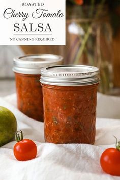 two jars filled with salsa sitting on top of a white towel next to an apple