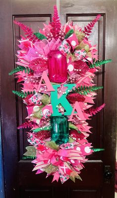 a pink and green wreath hanging on a door with a mason jar in the center