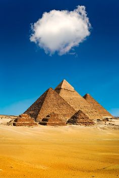 three pyramids in the desert under a blue sky with a white cloud above them