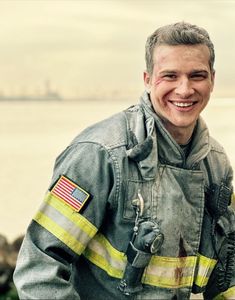 a firefighter is posing for a photo with his american flag on his chest and the water in the background