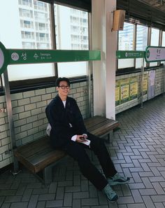 a man sitting on top of a wooden bench next to a train station wall covered in subway signs