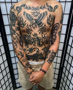 a man with tattoos standing in front of a tiled wall