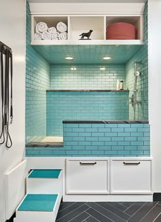 a bathroom with blue tile and white cabinets, black flooring and shelves filled with towels