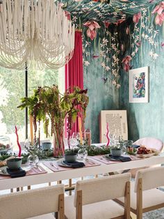 a dining room table is set with place settings and flowers on the wall behind it