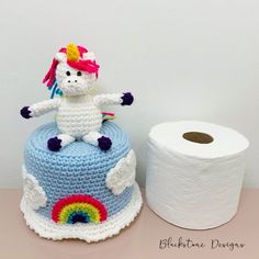 a crocheted unicorn sitting on top of a cake next to a roll of toilet paper