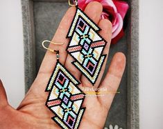 a hand holding a pair of beaded earrings in front of a box with flowers