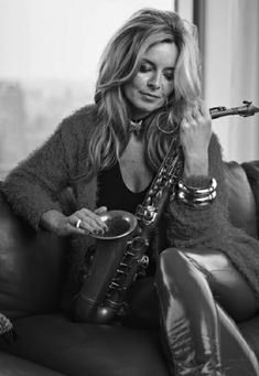 a woman sitting on top of a couch next to a window holding a saxophone in her hand