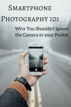 a person holding up a cell phone to take a photo on the road with fog in the background