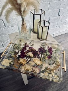 a glass table with flowers and candles on it next to a vase filled with feathers