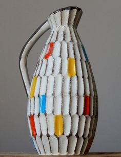 a white vase with multicolored lines on the outside and inside, sitting on a table