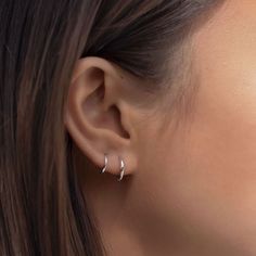 a close up view of a woman's ear with two small silver hoop earrings