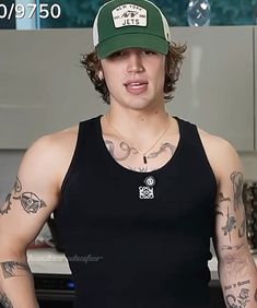 a man with tattoos and a black tank top is standing in front of a counter