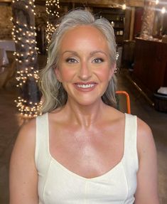 an older woman with grey hair smiling at the camera in front of some christmas lights