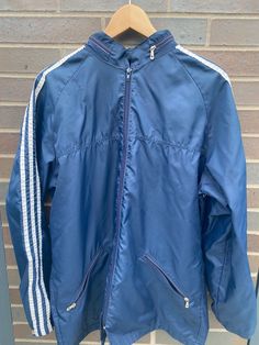 Vintage 1990s Adidas Windbreaker Navy Blue Jacket  - Length 30", Chest 22" - Used vintage condition - Hide-able hoodie - Perfect for spring/fall - 100% Nylon - Message for more information Please take note of the measurements listed as these are vintage clothes and may fit different than the tag size. Follow our page for more vintage clothing drops! Connect with us on Instagram: @recurarchives Sporty Nylon Outerwear With Three Stripes, Sporty Nylon Outerwear With Stripes, Long Sleeve Nylon Outerwear With Three Stripes, Athleisure Outerwear For Sports Events With Three Stripes, Athleisure Outerwear With Three Stripes For Sports, Sporty Nylon Outerwear For Sports Events, Nylon Track Jacket With Three Stripes For Sports, Sporty Nylon Track Jacket With Three Stripes, Athleisure Track Jacket For Sports Events