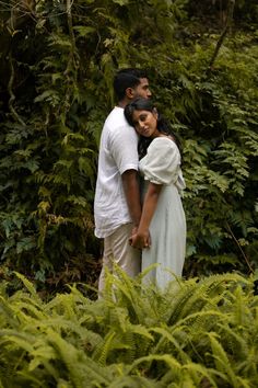 a man and woman standing next to each other in front of some trees with ferns