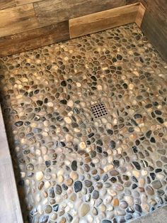 a shower with rocks on the floor and wooden wall behind it, along with a drain in the middle