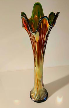 a colorful glass vase sitting on top of a white table next to a light colored wall