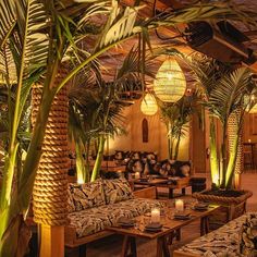 the interior of a restaurant with palm trees and couches in front of it,