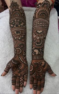 two hands with henna tattoos on them, one is showing the intricate pattern and the other has an elaborate design