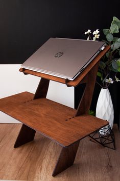 a laptop computer sitting on top of a wooden stand next to a vase with flowers