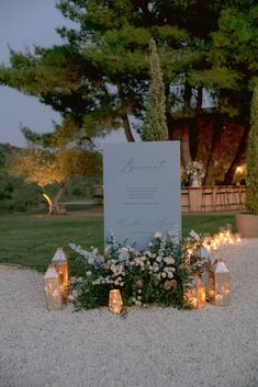 a wedding sign surrounded by candles in the middle of a gravel area with flowers and greenery