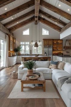 a living room filled with lots of furniture and wooden beams on the ceiling over looking an open kitchen