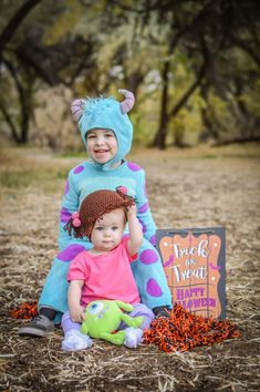 two children dressed up as monsters sitting on the ground in front of a trick or treat sign