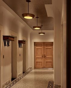 an empty hallway with two doors and three lights on either side of the door, leading to another room