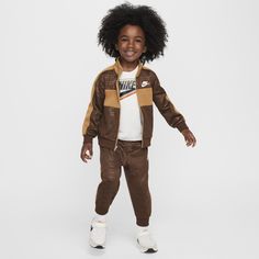 This statement-making tracksuit has style that will get your little one noticed on the playground and function that will help them stay comfy while they move. The jacket has a full-zip closure for easy layering, the standing collar adds extra coziness and pockets on the sides come in handy. The matching tapered pants have ribbed cuffs and a comfy elasticized waistband. Both pieces are enhanced with quick-drying, moisture-wicking Dri-FIT technology to help littles stay cool and dry while they play. Pair with any Nike tank or tee for a completed look. Sporty Long Sleeve Playtime Sets, Nike Tracksuit For Fall Sports, Nike Sporty Sports Sets, Casual Brown Playwear Sets, Nike Tracksuit For Sports, Fall Sports Sets Sportswear, Casual Nike Tracksuit For Fall, Fall Sportswear Sets For Sports, Sporty Sets For Fall Sports