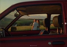 two people standing in the drivers seat of a red truck