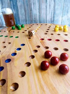 a wooden board game with dices and balls on the table next to a glass of beer