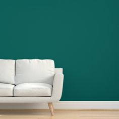 a white couch against a teal green wall in an empty room with wooden floors