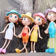 five dolls are standing next to each other in front of a tree trunk, wearing hats and dresses