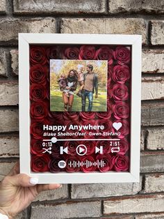 a hand holding up a framed photo with the words happy anywhere and two people standing next to each other