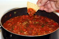 a person dipping tortilla chips into a pot of chili