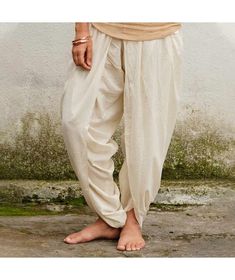 This relaxed fit ladies white dhoti pant gently combines usefulness and style. These pants, custom designed for women, are sleeker and well fitted. With convenient drawstring fasteners at the waist that can be fastened at the sides, for a fuss-free look. No elastic at the waistband for a cleaner finish and better comfort. Suitable for yoga practices as well as everyday wear it allows you to combine the utmost comfort with that inimitable Isha style. White Ankle-length Harem Pants With Loosely Fitted Hips, White Loose Fit Ankle-length Harem Pants, White Relaxed Fit Harem Pants With Elastic Waistband, White Cotton Ankle-length Harem Pants, White Cotton Relaxed Fit Harem Pants, White Cotton Tapered Leg Harem Pants, Traditional White Bottoms, Traditional White Long Pants, White Harem Pants For Yoga In Summer