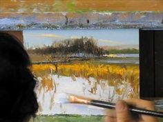 a person holding a paintbrush in front of an easel with paintings on it