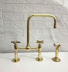 two brass faucets on a white countertop against a brick wall, one is turned off