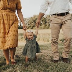 a man and woman holding hands while walking with a toddler on the grass in front of them