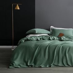 a bed with green sheets and pillows in a dark room next to a floor lamp