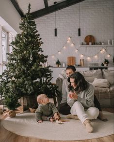 a woman sitting on the floor next to a baby in front of a christmas tree