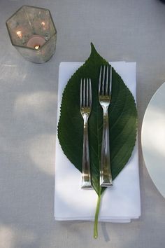 two forks are placed on a napkin with a green leaf as the centerpieces