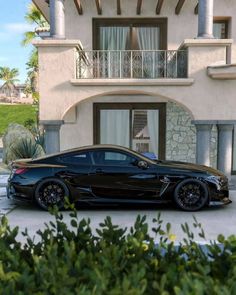 a black sports car parked in front of a house with palm trees and bushes around it