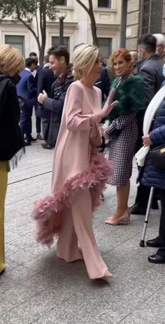 two women in pink dresses are walking down the street with other people standing around them