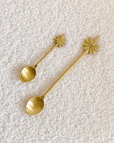 two gold spoons with flowers on them sitting on a white carpeted floor next to each other