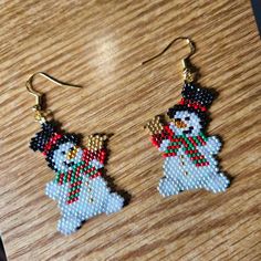 a pair of beaded snowman earrings sitting on top of a wooden table