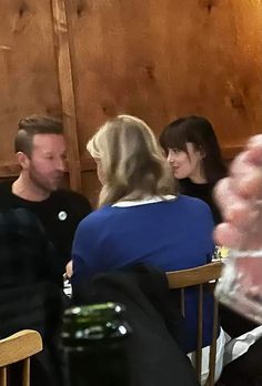 three people sitting at a table talking to each other in a room with wood paneled walls