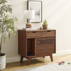 a wooden cabinet with two drawers and a lamp on top next to a potted plant