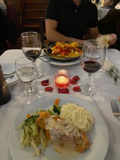 a man sitting at a table in front of a plate of food and wine glasses