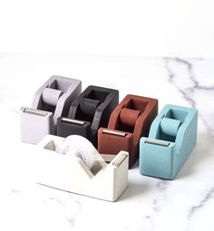 four different colored toilet paper holders sitting on a marble counter top next to each other